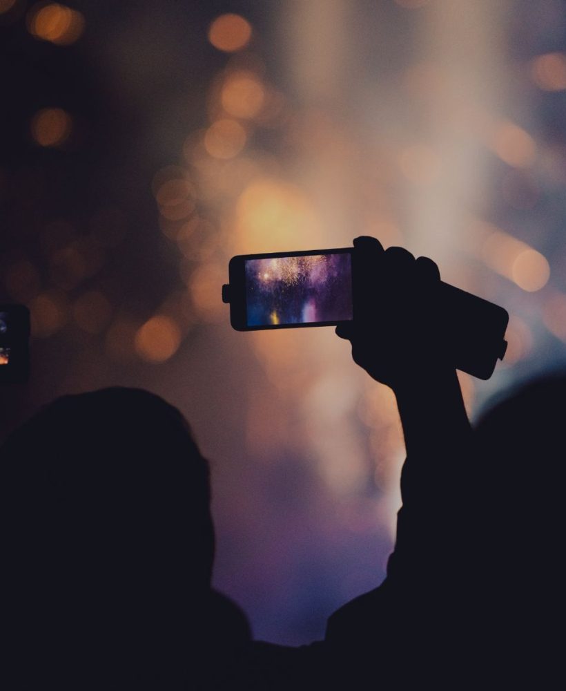 An image of a person videoing an event using a camera on a phone.