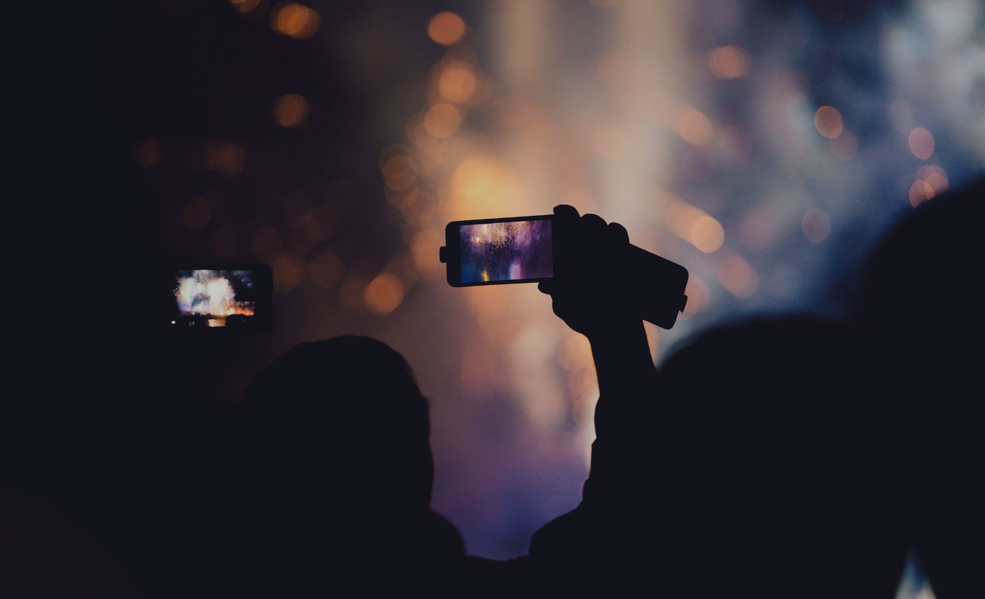 An image of a person videoing an event using a camera on a phone.